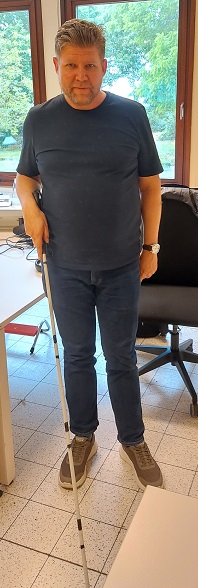 Een man met visuele Handicap demonstreert de Witte Stok; hij houdt de stok voor zich met de rechterhand.